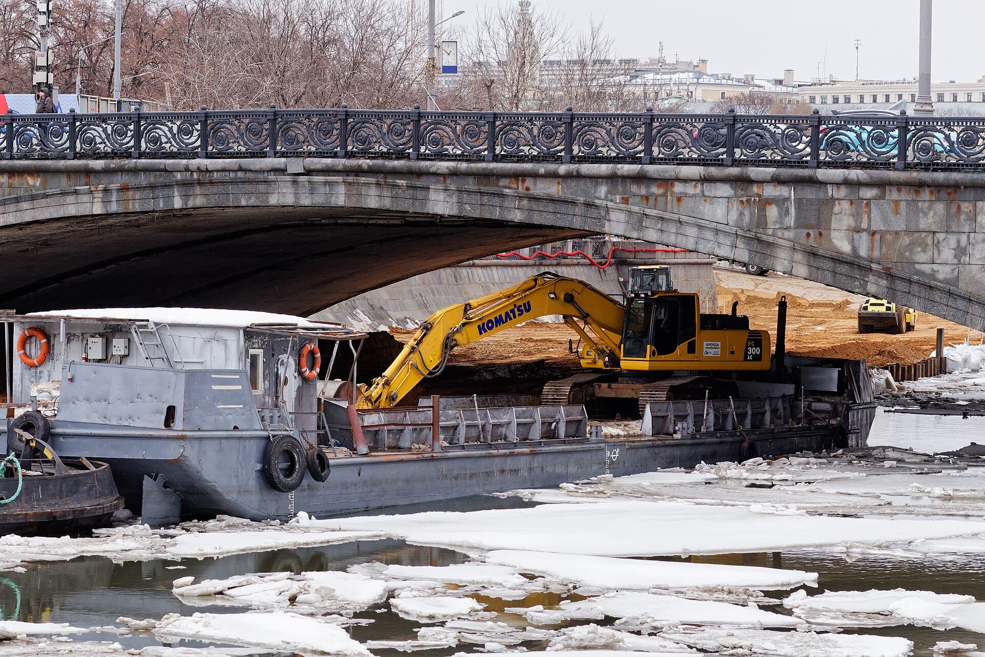 Excavator performing earthworks beside a stone bridge