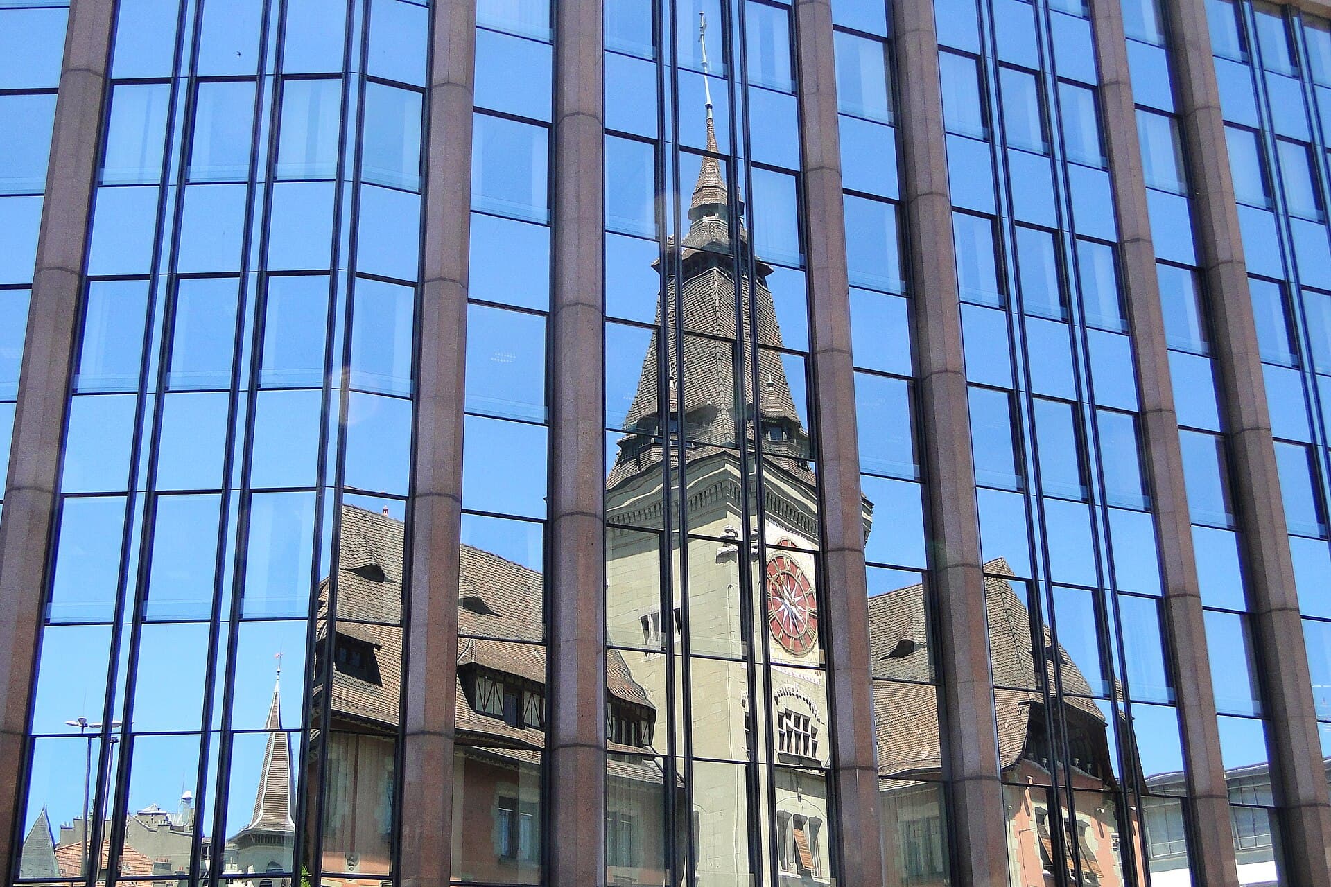 Modern glass curtain-wall facade reflecting a historic clock tower
