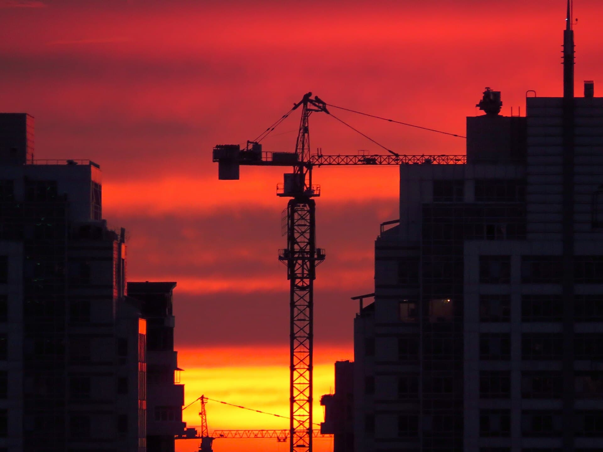 Tower cranes silhouetted against a golden sunset over a city under construction