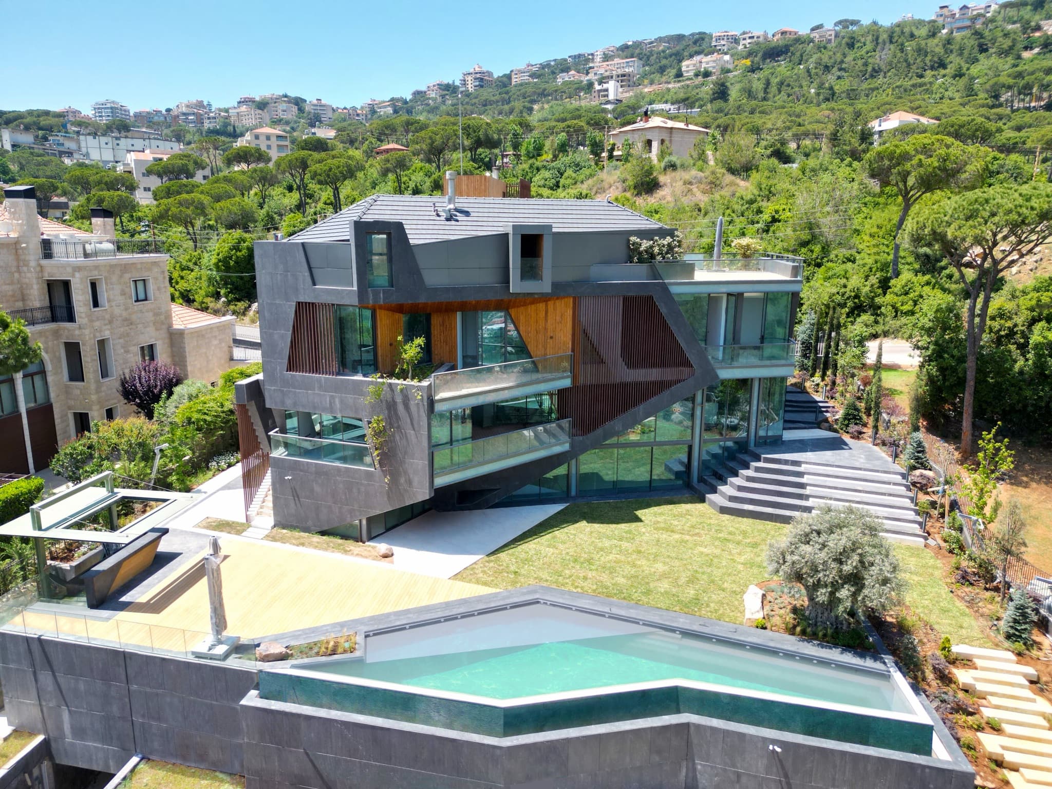 Striking modern luxury residence with glass facades and a terraced pool deck on a wooded hillside